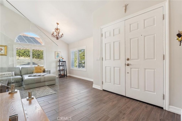 foyer entrance with dark wood-style floors, vaulted ceiling, a chandelier, and baseboards