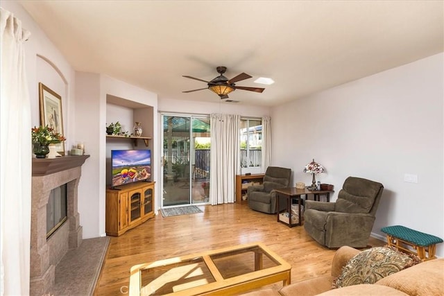 living area featuring a ceiling fan, a premium fireplace, and wood finished floors