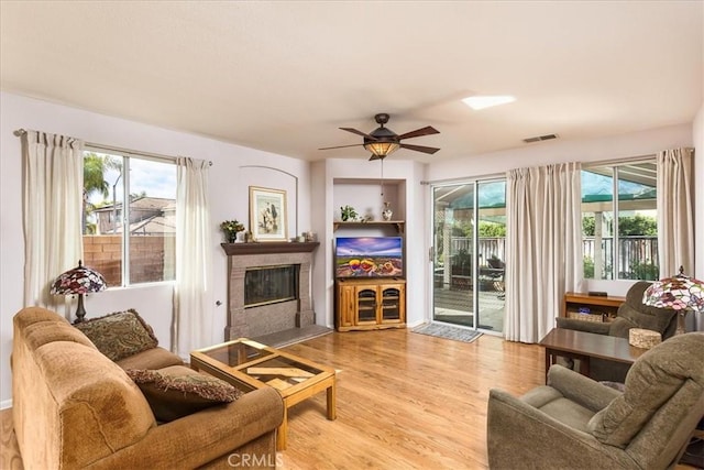 living area with a glass covered fireplace, a healthy amount of sunlight, visible vents, and wood finished floors