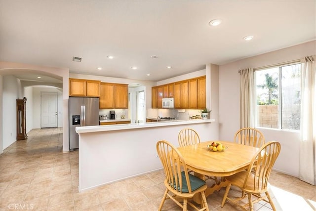 kitchen with arched walkways, light countertops, visible vents, white microwave, and stainless steel fridge with ice dispenser