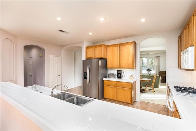 kitchen with white appliances, visible vents, tile counters, arched walkways, and a sink