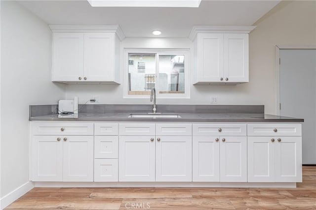 kitchen featuring baseboards, white cabinets, dark countertops, light wood-style floors, and a sink