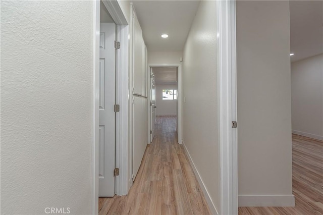 corridor with light wood-type flooring, baseboards, and a textured wall