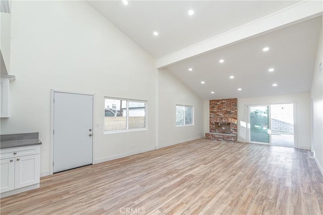 unfurnished living room featuring high vaulted ceiling, recessed lighting, a fireplace, and light wood-style flooring