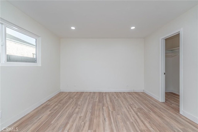 unfurnished bedroom featuring baseboards, recessed lighting, a walk in closet, and light wood-style floors