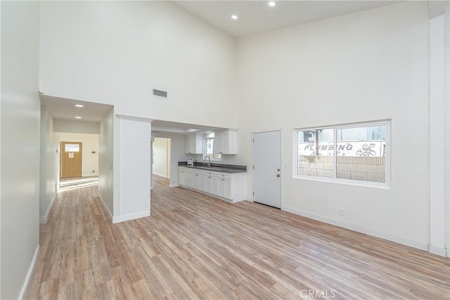 unfurnished living room with baseboards, visible vents, light wood-type flooring, a sink, and recessed lighting