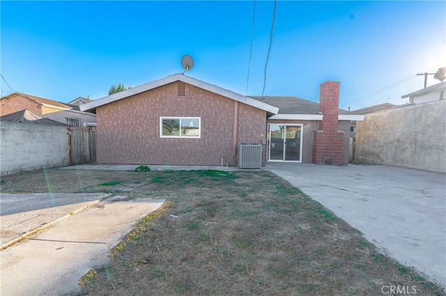 rear view of property featuring a patio, a chimney, central air condition unit, stucco siding, and fence