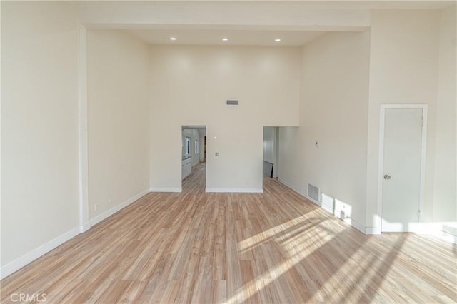 empty room featuring recessed lighting, visible vents, light wood-style flooring, a towering ceiling, and baseboards