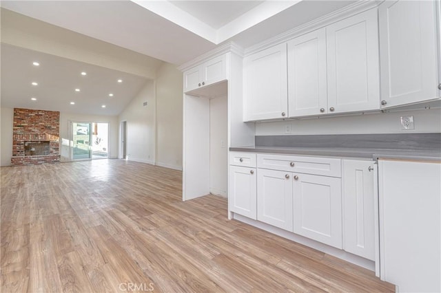 kitchen with vaulted ceiling with beams, light wood finished floors, a brick fireplace, and white cabinetry