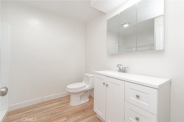 bathroom with toilet, wood finished floors, vanity, and baseboards