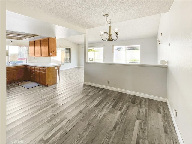 kitchen with a chandelier, wood finished floors, baseboards, vaulted ceiling, and brown cabinets