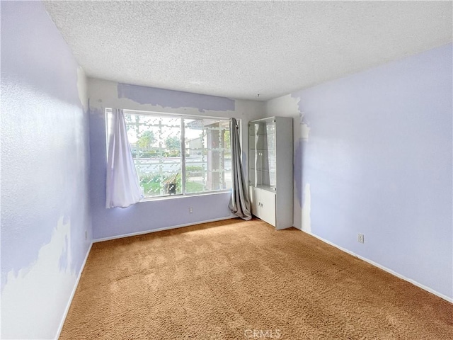 spare room with a textured ceiling, baseboards, and light colored carpet