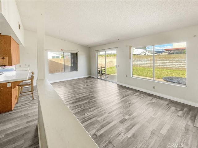 unfurnished living room with light wood-style flooring, baseboards, vaulted ceiling, and a textured ceiling