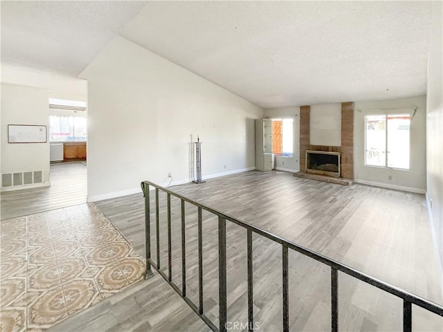 unfurnished living room with a large fireplace, baseboards, visible vents, lofted ceiling, and wood finished floors