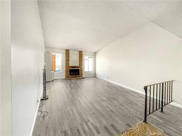 unfurnished living room with a fireplace, a textured ceiling, baseboards, and wood finished floors