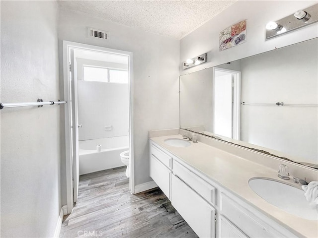 full bath with toilet, a textured ceiling, visible vents, and a sink