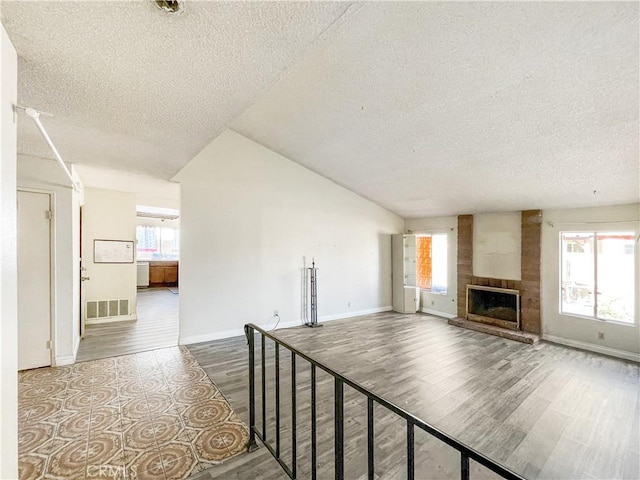 unfurnished living room featuring wood finished floors, a large fireplace, visible vents, and a healthy amount of sunlight