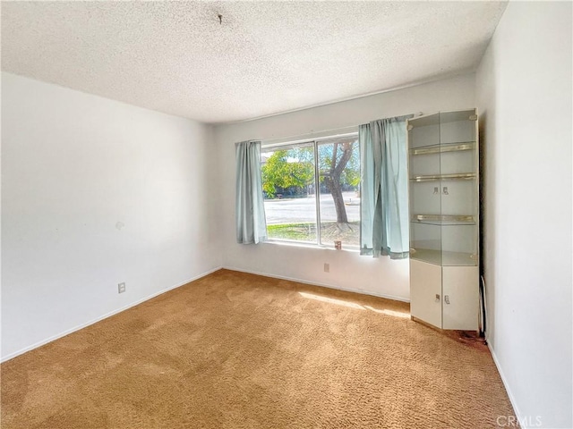 carpeted spare room with a textured ceiling and baseboards