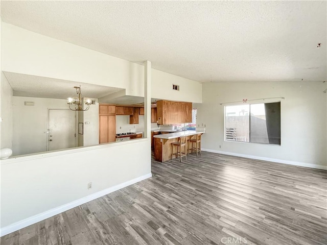 unfurnished living room featuring a textured ceiling, a notable chandelier, wood finished floors, baseboards, and vaulted ceiling