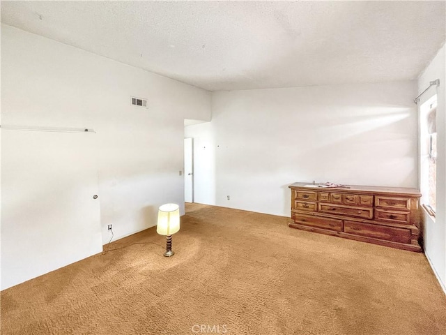 spare room featuring carpet, visible vents, lofted ceiling, and a textured ceiling