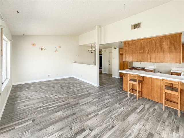 kitchen featuring visible vents, tile counters, brown cabinets, wood finished floors, and vaulted ceiling