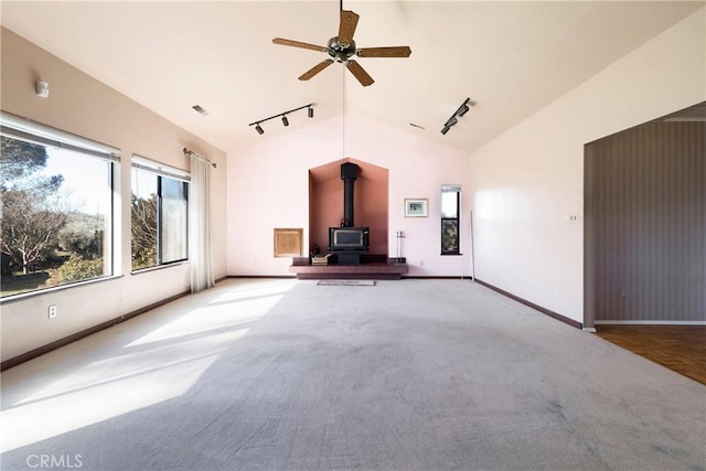 unfurnished living room featuring track lighting, a wood stove, ceiling fan, carpet flooring, and vaulted ceiling