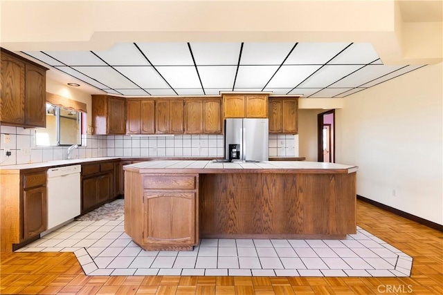 kitchen featuring backsplash, white dishwasher, a center island, stainless steel fridge, and tile counters