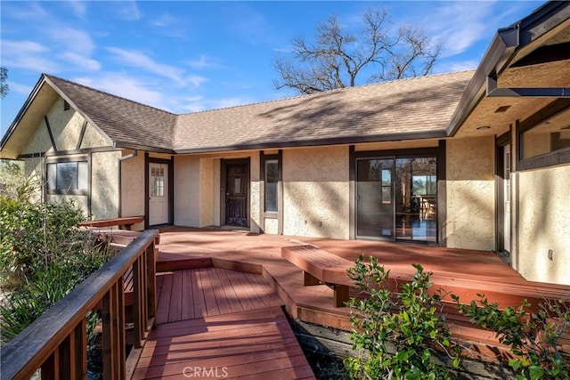 back of property with a shingled roof, stucco siding, and a deck