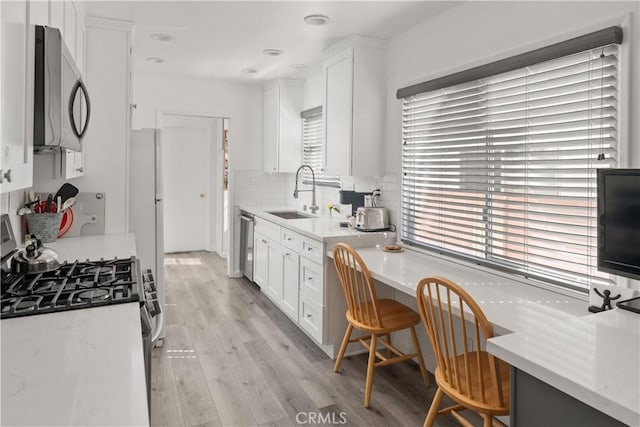 kitchen with light wood finished floors, backsplash, appliances with stainless steel finishes, white cabinets, and a sink