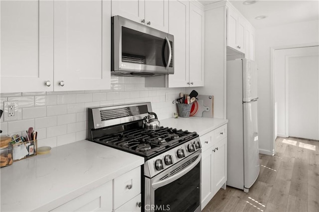 kitchen with stainless steel appliances, light wood finished floors, white cabinetry, and tasteful backsplash