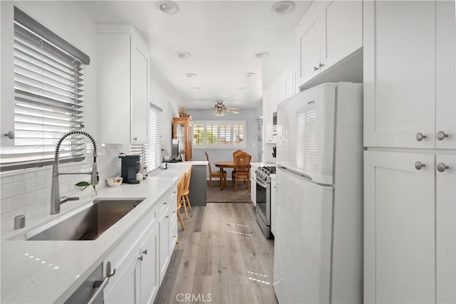 kitchen with stainless steel gas range, a sink, freestanding refrigerator, and white cabinetry