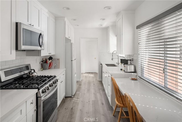 kitchen with light wood-style flooring, a sink, white cabinetry, appliances with stainless steel finishes, and backsplash