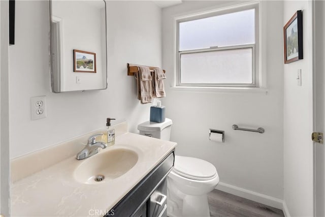 half bath with toilet, baseboards, wood finished floors, and vanity