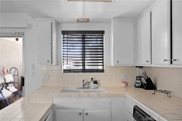 kitchen featuring tile countertops, tasteful backsplash, white cabinetry, and a sink