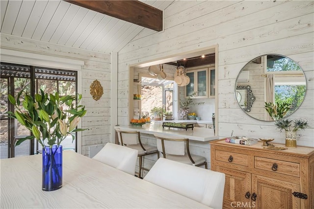 dining space featuring vaulted ceiling with beams and wooden walls