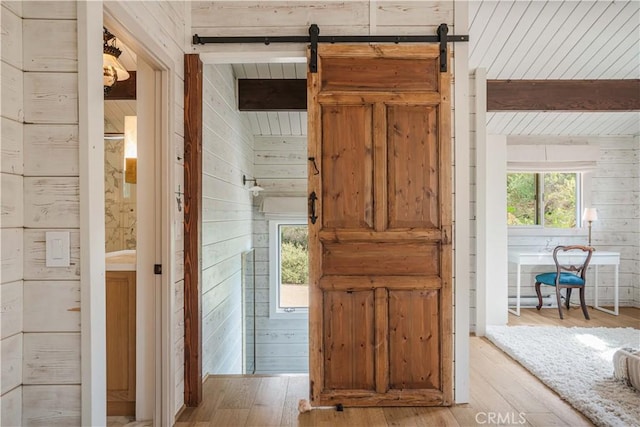 hallway featuring beam ceiling, light wood-style flooring, a barn door, wood walls, and wooden ceiling