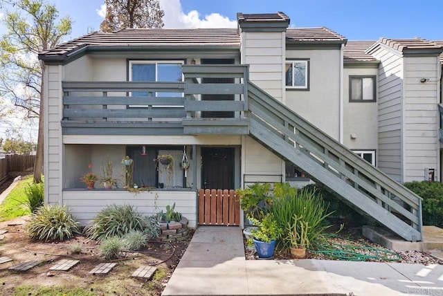 townhome / multi-family property with a tile roof, fence, a balcony, and stairs