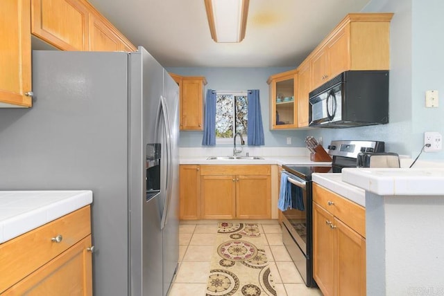 kitchen featuring tile countertops, light tile patterned floors, appliances with stainless steel finishes, glass insert cabinets, and a sink