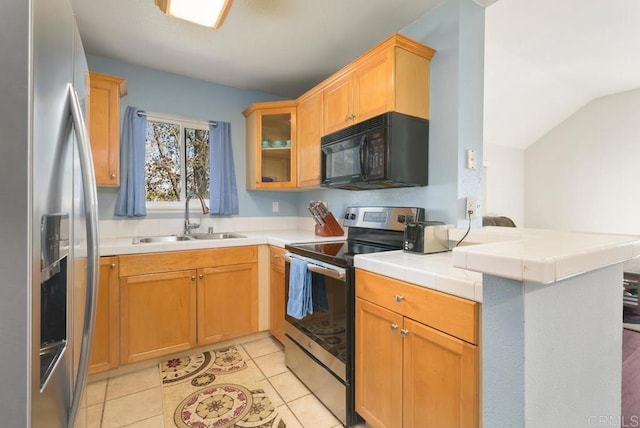 kitchen with lofted ceiling, appliances with stainless steel finishes, glass insert cabinets, a peninsula, and a sink