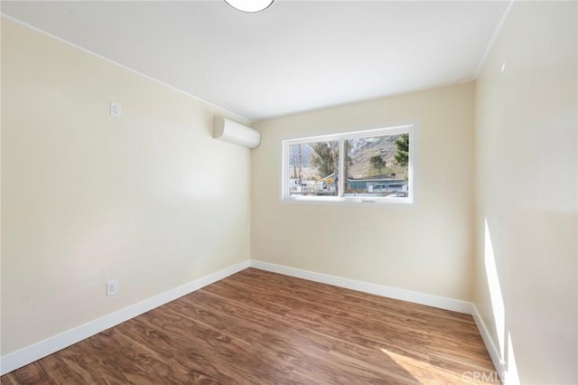 spare room featuring a wall unit AC, baseboards, and wood finished floors