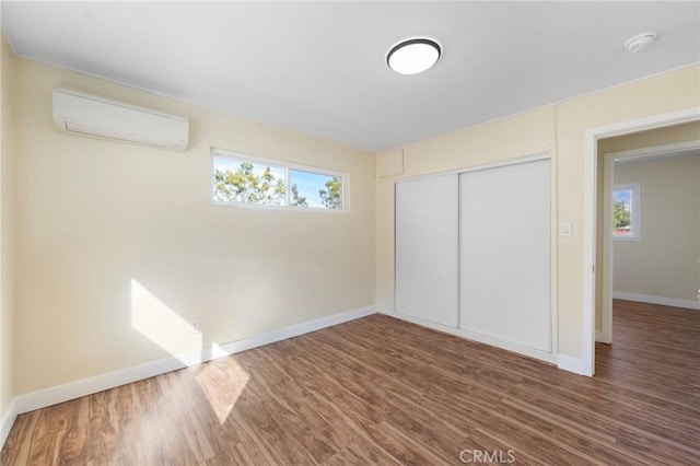 unfurnished bedroom featuring a closet, baseboards, wood finished floors, and a wall mounted AC