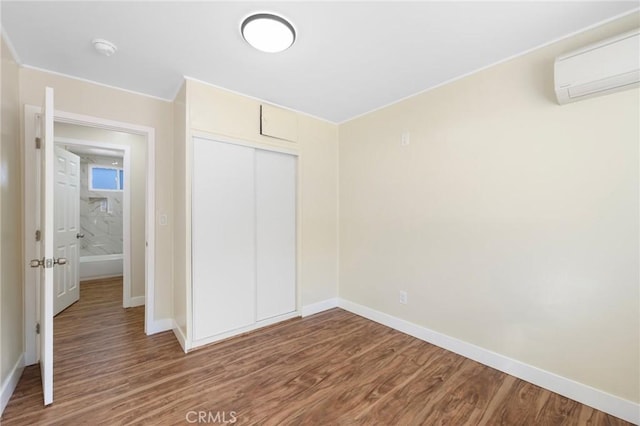 unfurnished bedroom featuring a wall mounted air conditioner, baseboards, and wood finished floors