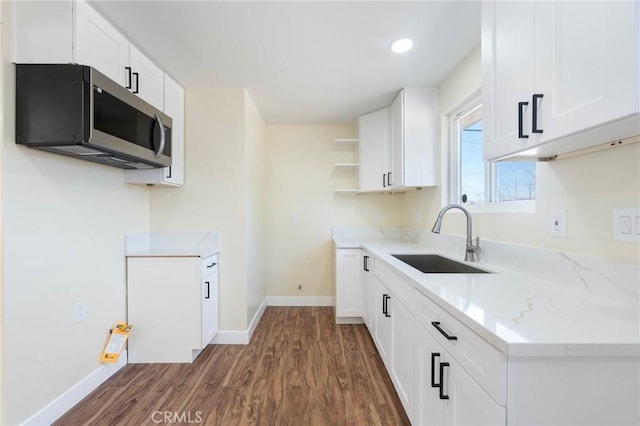 kitchen with dark wood finished floors, light stone counters, stainless steel microwave, open shelves, and a sink