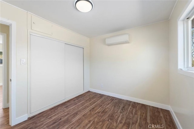 unfurnished bedroom featuring dark wood-type flooring, a closet, baseboards, and a wall mounted AC