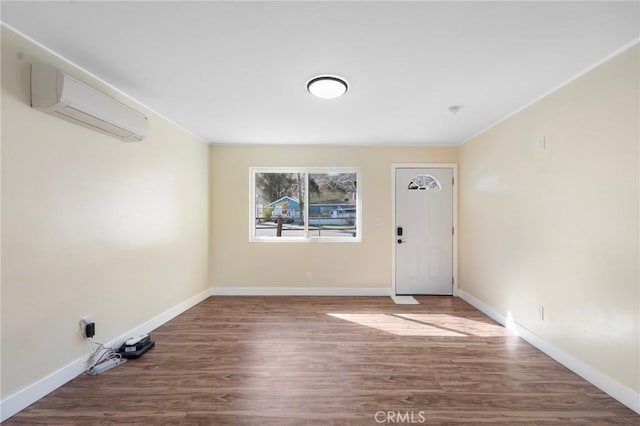 spare room with a wall unit AC, baseboards, and wood finished floors