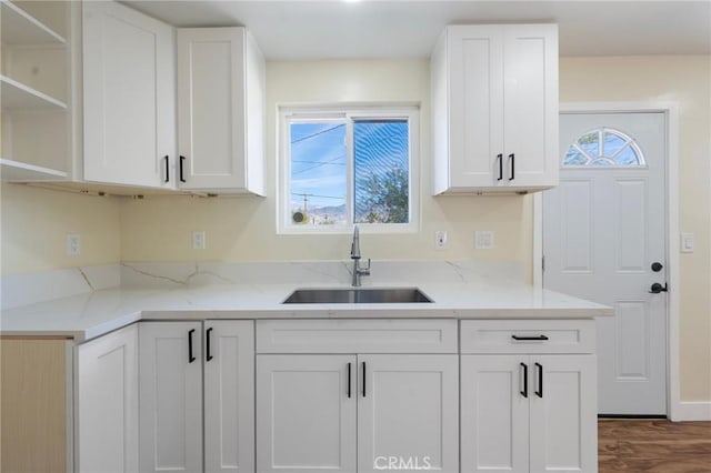 kitchen with wood finished floors, a sink, white cabinetry, light stone countertops, and open shelves