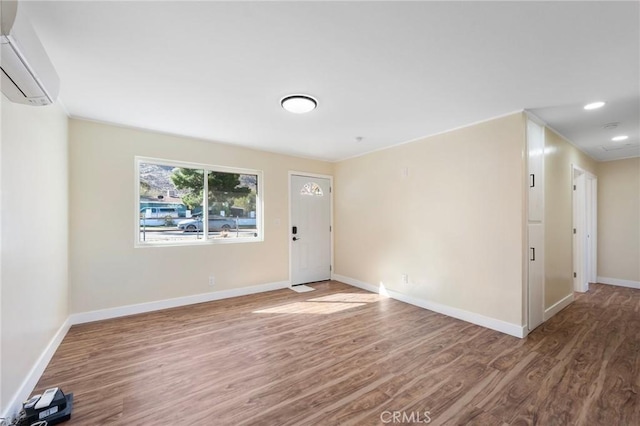 interior space with recessed lighting, a wall unit AC, baseboards, and wood finished floors