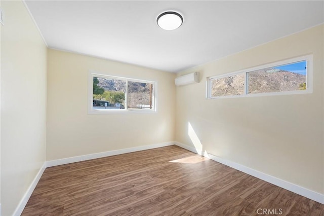 unfurnished room with a wall mounted air conditioner, wood finished floors, and baseboards