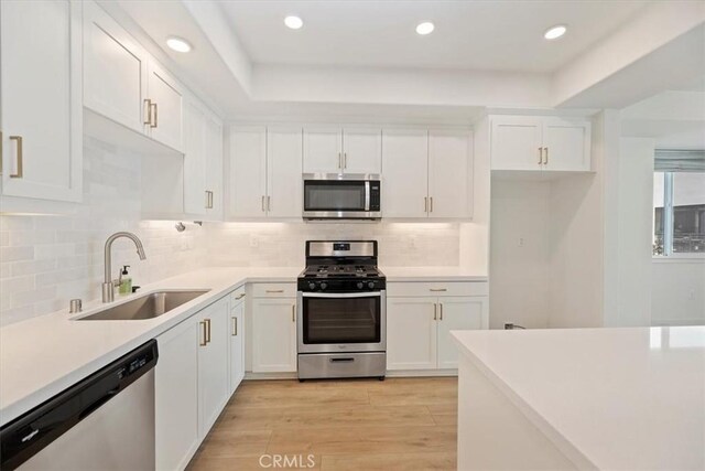 kitchen with stainless steel appliances, light countertops, white cabinets, a sink, and light wood-type flooring