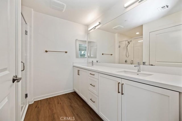 bathroom featuring double vanity, visible vents, a stall shower, a sink, and wood finished floors